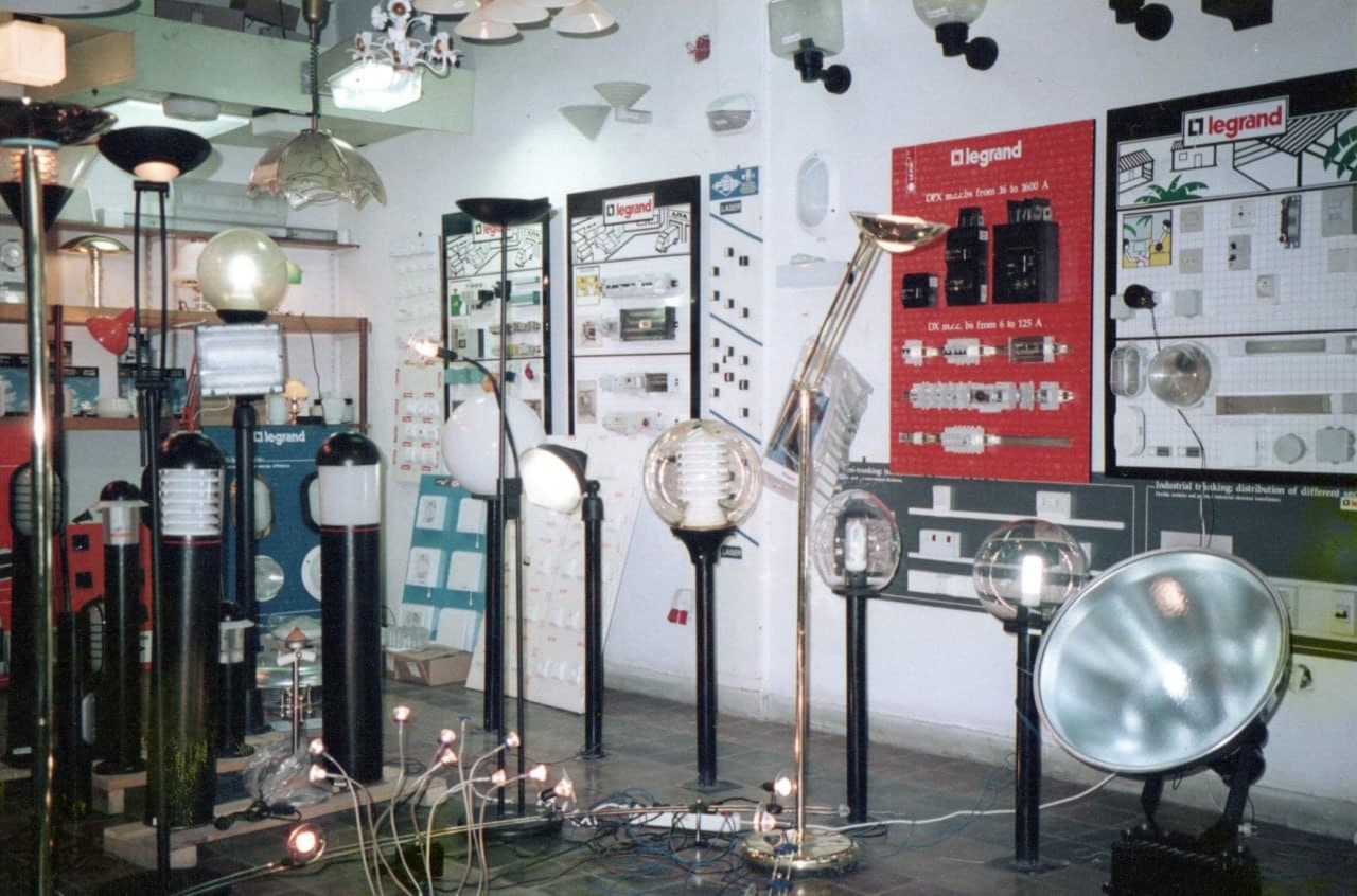 The showroom floor: standard lamps and globe fittings lit, Legrand display boards on the wall behind