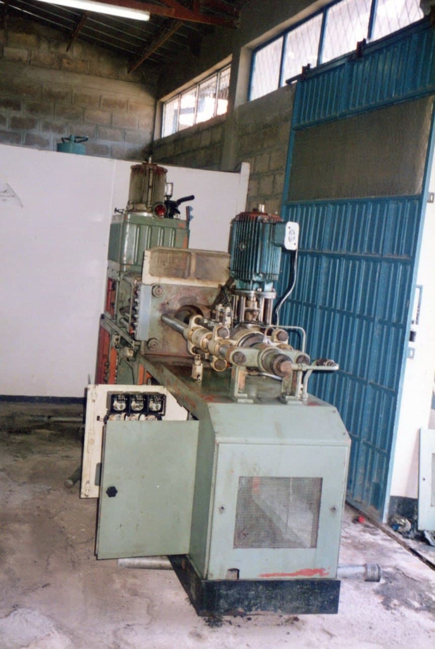 The same machine end on, under a high workshop window, the blue shutter door beside it