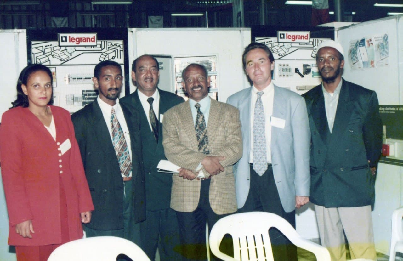Six people at a trade stand, Legrand boards and a switchgear cabinet behind them